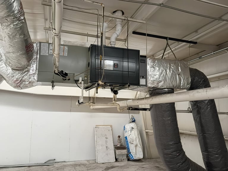 Ceiling-mounted HVAC system with black ductwork and insulation in an empty room with white walls