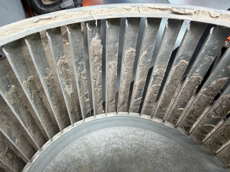 Close-up of a dusty turbine fan with multiple curved metal blades arranged in a radial pattern