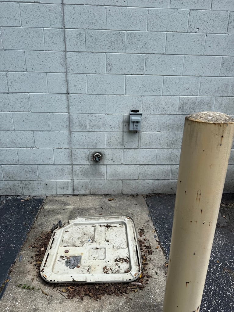 Weathered concrete wall with electrical outlet, metal utility cover in ground, and yellow pipe