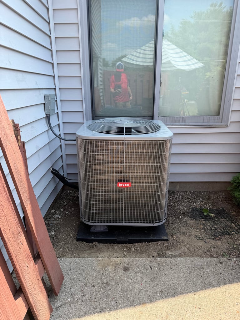 Air conditioning unit installed outside a house with white siding and large patio doors in the background