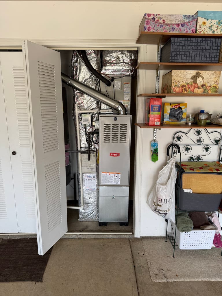 Open utility closet showing HVAC system with furnace and ductwork, next to shelving unit with storage boxes and household items