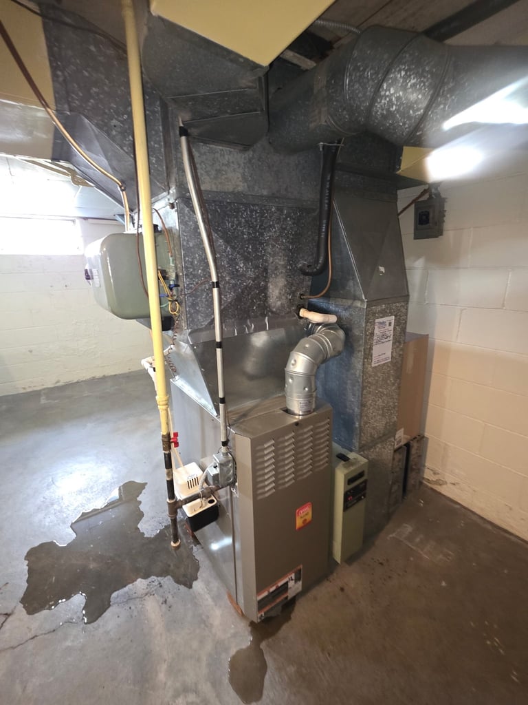 HVAC furnace unit in basement with ductwork and insulation, mounted against concrete wall