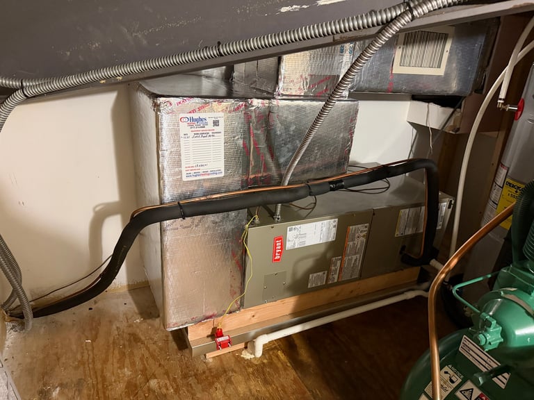 HVAC furnace unit mounted on basement wall with ductwork, wiring, and foam insulation visible