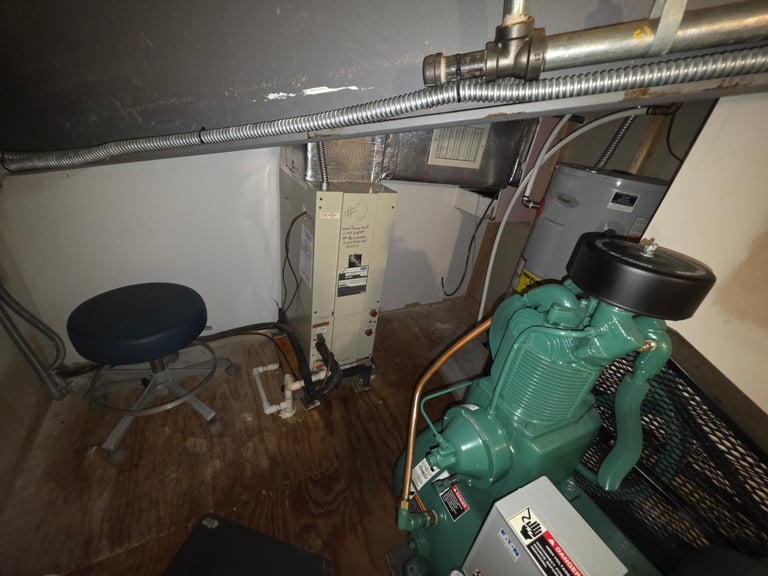 Basement utility room with green water pump, metal pipes, white HVAC unit, and a black stool on wooden floor