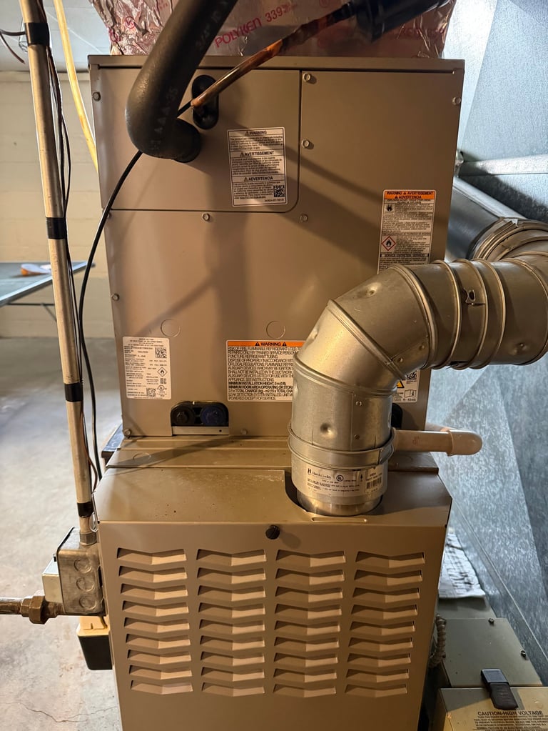Tan and brown HVAC furnace unit with ductwork, control panels, and louvered base in basement or utility space