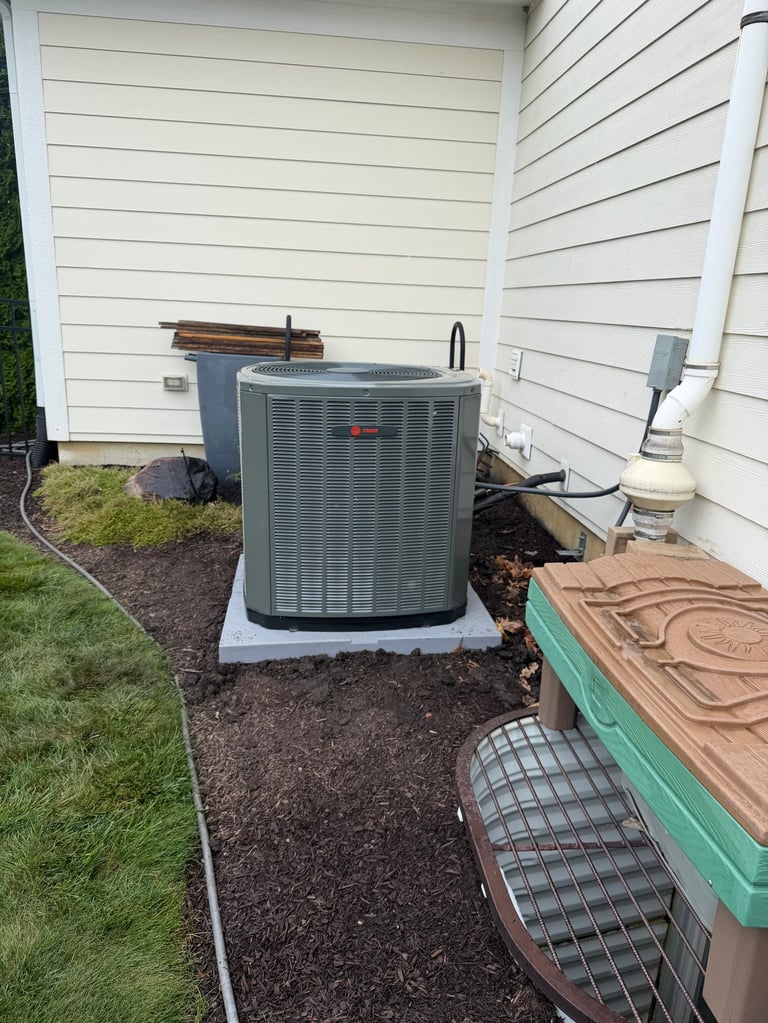 HVAC air conditioning unit mounted on concrete pad beside white house with mulched ground and storage containers nearby