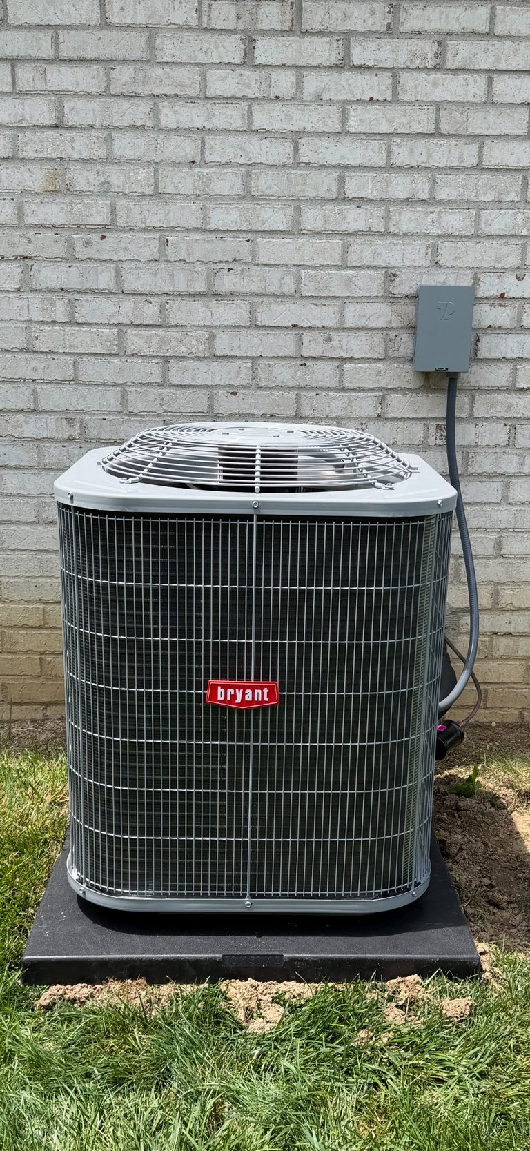 Bryant air conditioning unit installed against a white brick wall with electrical box and power cord