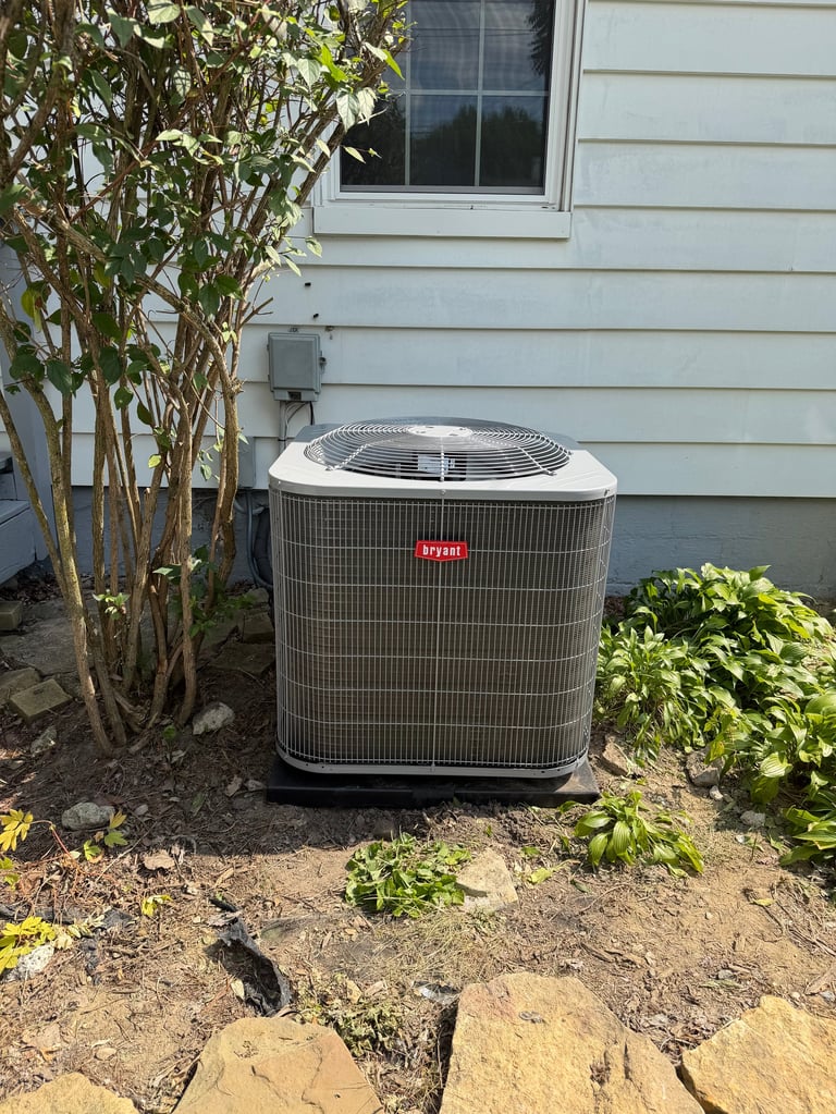Outdoor air conditioning unit against a house wall surrounded by landscaping and shrubs