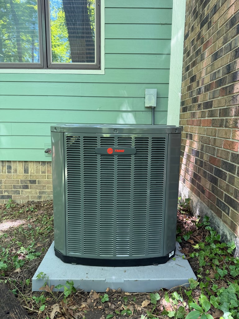 Green HVAC air conditioning unit installed against brick and green siding on concrete pad beside residential home