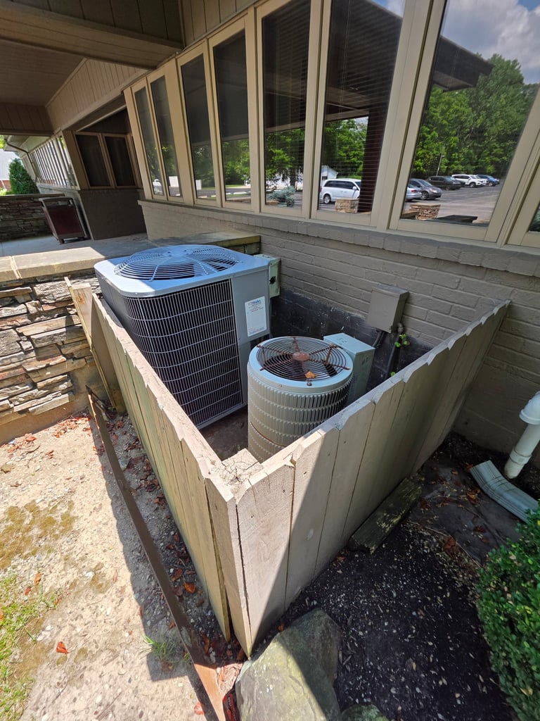 HVAC units enclosed in wooden fence on building exterior with parking lot visible through large windows