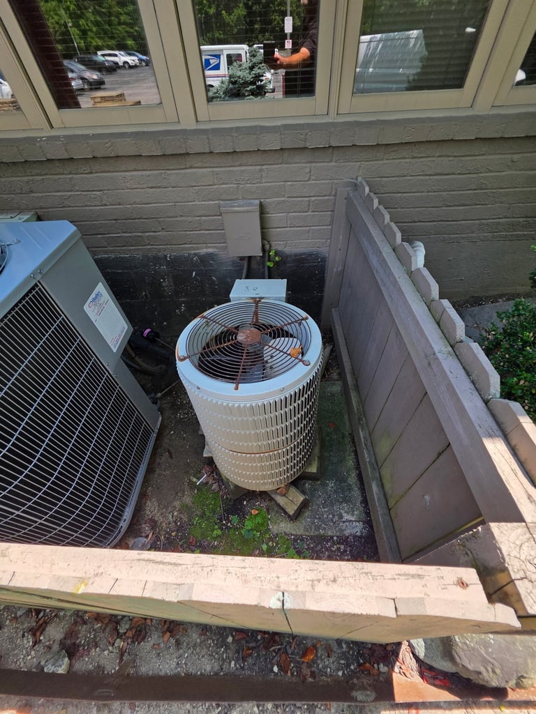 HVAC units in outdoor enclosure next to brick building wall with windows