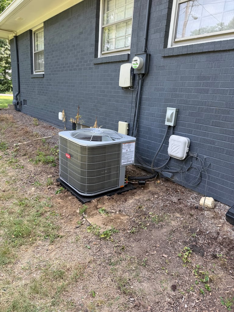 Outdoor HVAC unit installed against a dark blue brick house exterior with electrical connections and ground-level placement