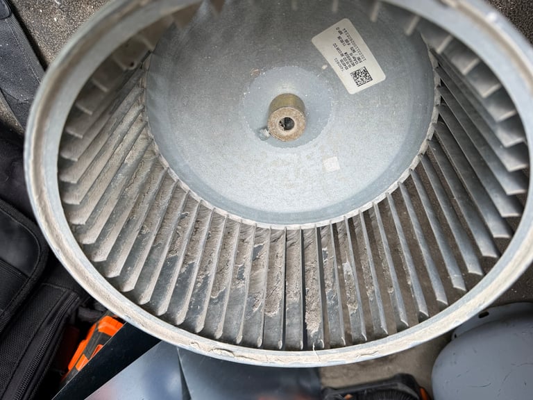 Close-up of a circular HVAC blower wheel with metal fins and a center hub, showing dust accumulation