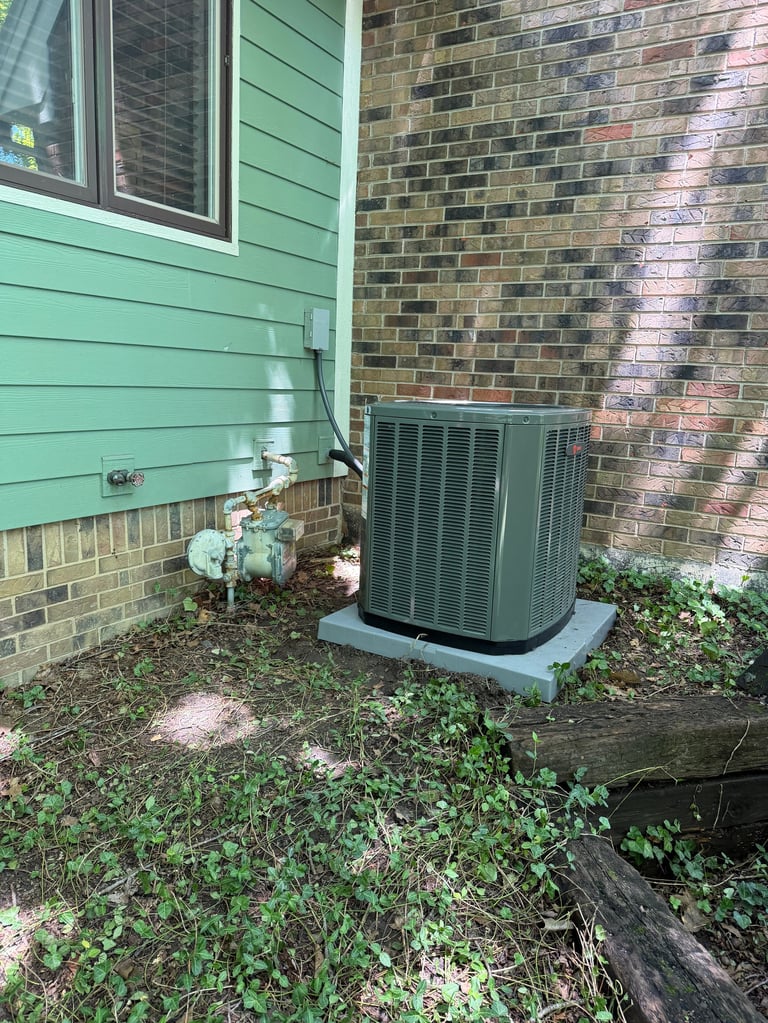 Green HVAC air conditioning unit installed outside a house with brick and green siding walls